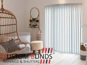 Custom Blinds Shutters & Awnings South Africa A stylish lounge with vertical blinds on patio doors, chic decor, and hanging chair—easy shade for sunny SA living. Custom Blinds logo. Garden Route & Online