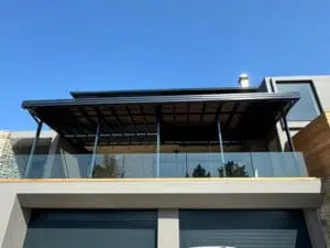 Custom Blinds South Africa Stylish double-storey home with a spacious glass balcony and large louvred awning offering Simola Knysna shade and stunning views on sunny days. Garden Route & Online