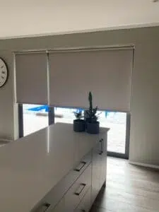 Custom Blinds Shutters & Awnings South Africa Bright kitchen with a white island and plants; blockout roller blinds filter the sun, offering pool views and privacy at home. Garden Route & Online