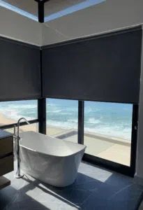 Custom Blinds Shutters & Awnings South Africa A sleek bathroom with a freestanding bath and blockout roller blinds for this Glentana beach front, George home, giving privacy and stunning beach views at home. Garden Route & Online