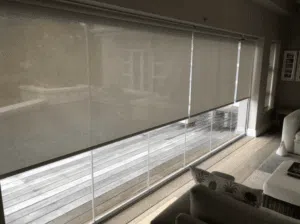 Custom Blinds Shutters & Awnings South Africa see roller blinds cover tall windows, bringing shade and style to a lounge that opens onto a wooden patio and lush outdoors. taken in George Garden Route & Online