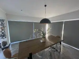 Custom Blinds Shutters & Awnings South Africa A stylish dining room with sleek blackout roller blinds in grey, inviting privacy and comfort whilst soft natural Knysna light streams in. Garden Route & Online
