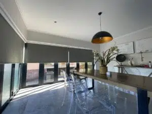 Custom Blinds Shutters & Awnings South Africa Bright dining space with blackout roller blinds, stylish table and chairs—perfect for privacy and a warm, inviting Knysna atmosphere. Garden Route & Online