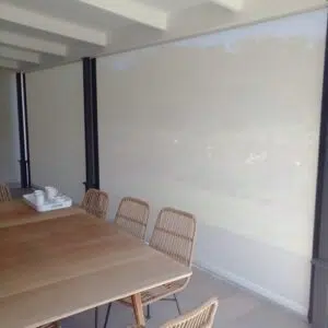 Custom Blinds Shutters & Awnings South Africa A stylish Plettenberg Bay patio with a wooden table and wicker chairs; outdoor blinds let in soft light, making the space calm and perfect for relaxing. Garden Route & Online