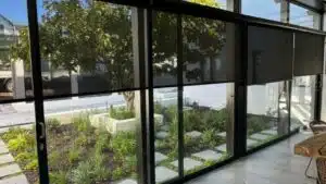 Custom Blinds Shutters & Awnings South Africa Sleek black roller blinds on big windows frame a leafy Belvidere. Knysna garden, adding privacy and style to your home’s living space. Garden Route & Online