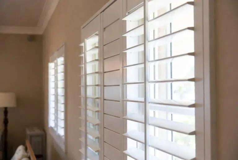 Full wall PVC indoor shutters in a Knysna apartment with lagoon light, white louvres open for ventilation