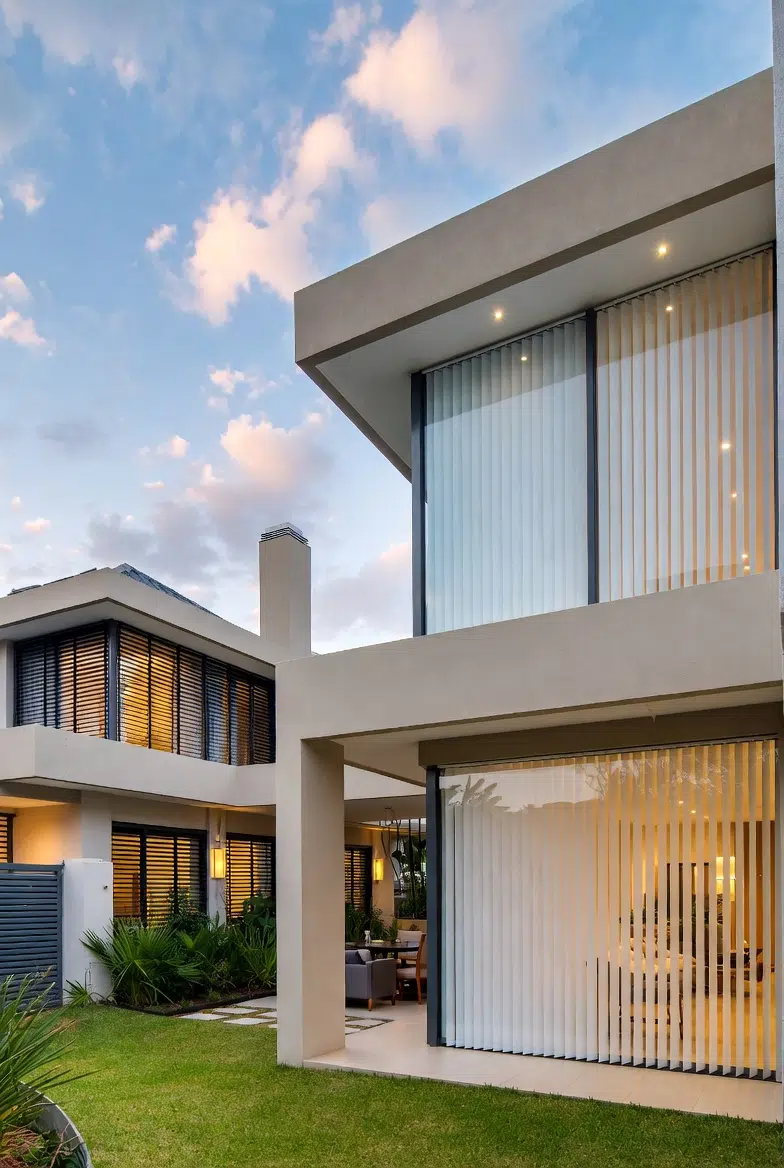 Contemporary home at dusk with vertical blinds on wide glazing, warm interior lighting visible