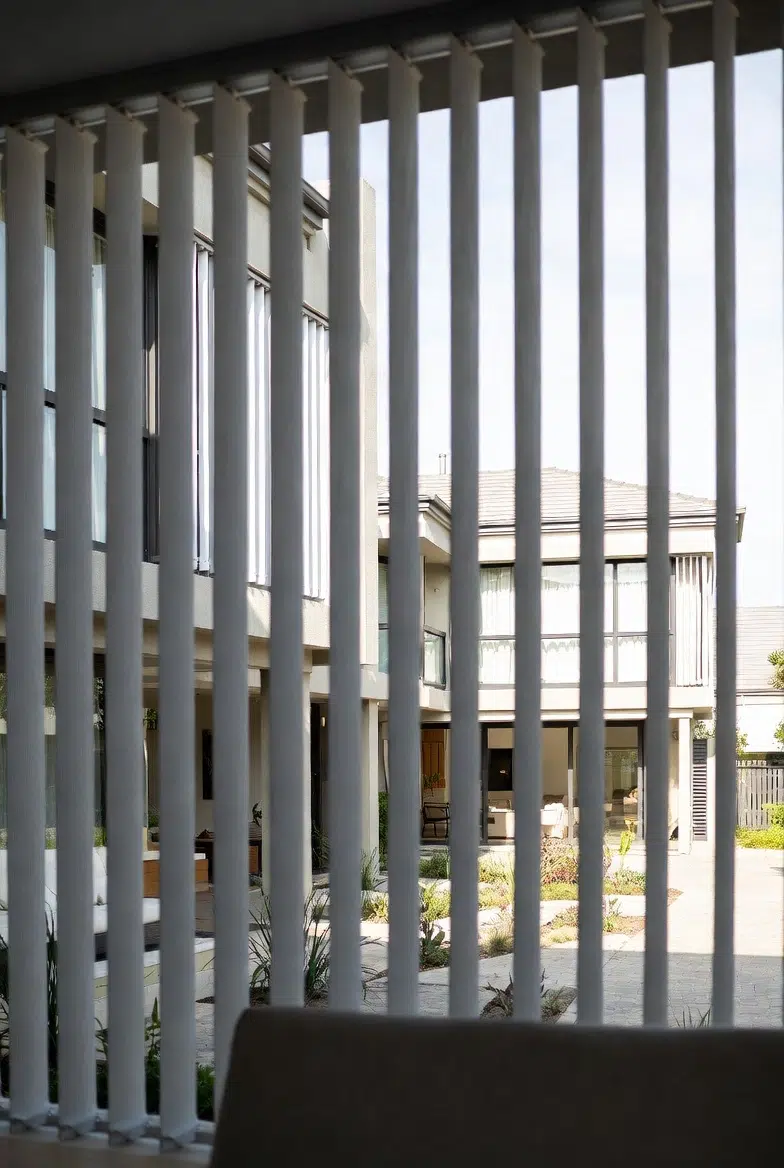White vertical blinds viewed from inside looking through to courtyard garden, light filtering through louvres