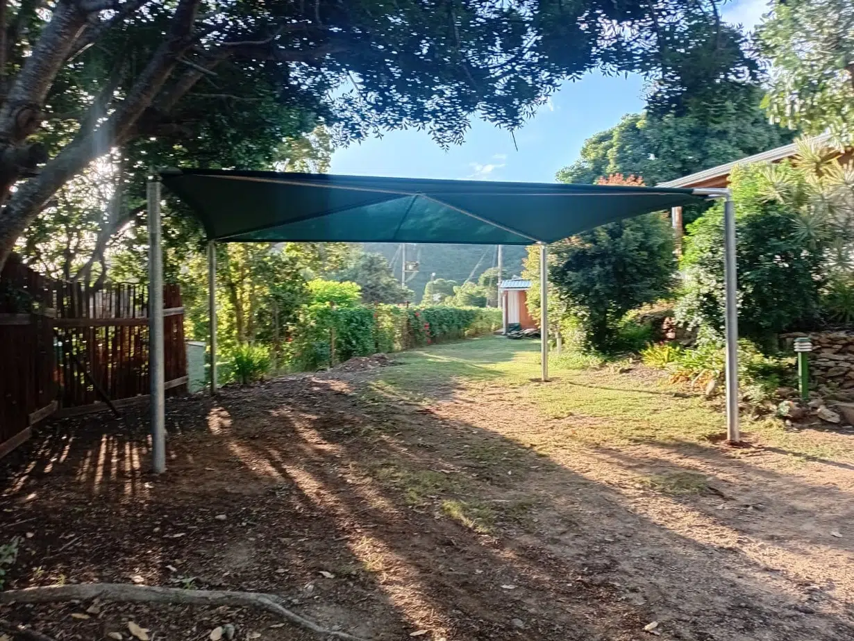 Shadeport with galvanised steel frame and green shade cloth in Wilderness, showing garden setting with indigenous trees. Custom Blinds Garden Route.