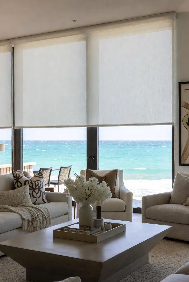 Sheer roller blinds in a coastal lounge with turquoise ocean view and neutral decor