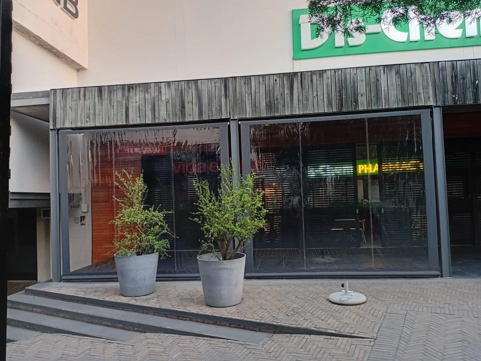 Exterior view of clear PVC blinds at Vida e Cafe Knysna Mall with Dis-Chem signage above, fully enclosing the outdoor seating terrace
