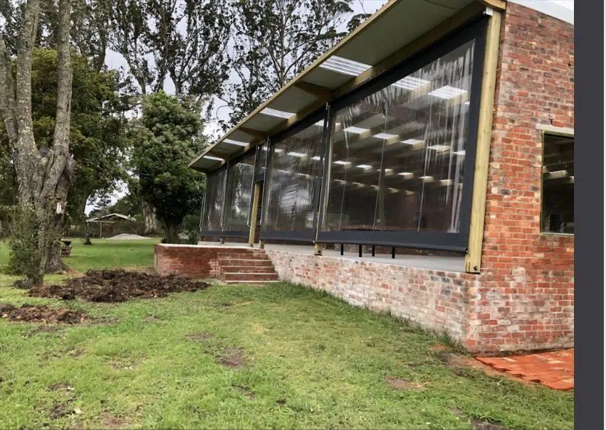 Clear PVC drop-down outdoor blinds installed at Luka Vineyards, Garden Route. Designed and manufactured by Custom Blinds with dark grey side channels on a brick and timber pergola.