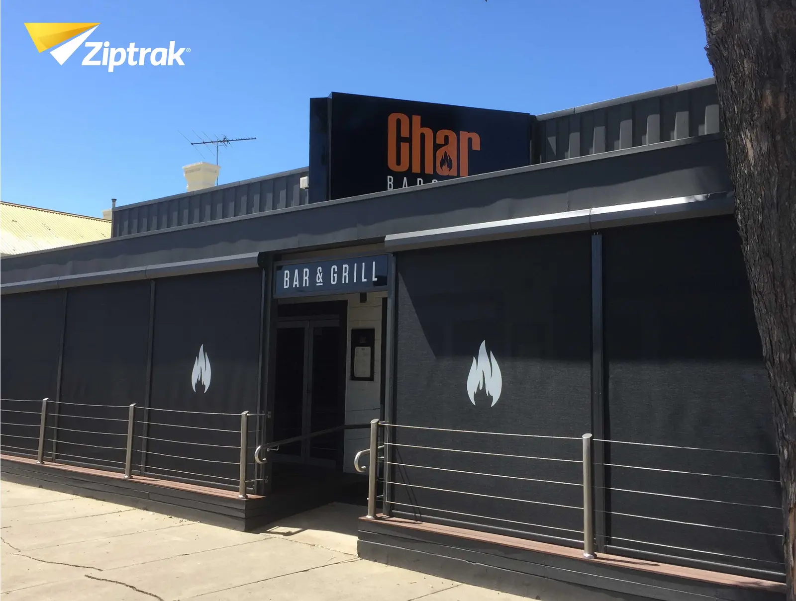 Ziptrak outdoor blinds in commercial restaurant application, full charcoal mesh wrap with branded fabric panels creating extended outdoor dining space, supplied by Custom Blinds authorised Ziptrak retailer Garden Route