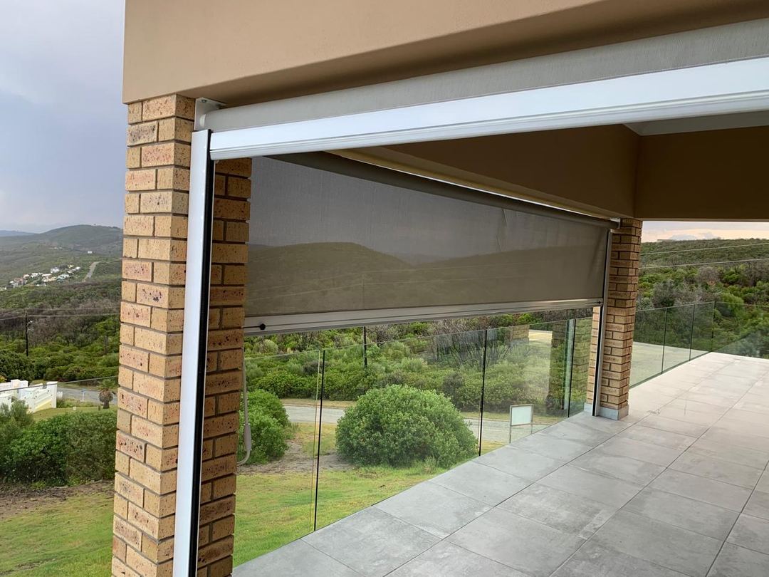 Sidetrack outdoor blind in grey screen mesh, half lowered between brick pillars in its aluminium side channels, by Custom Blinds Shutters & Awnings, Knysna