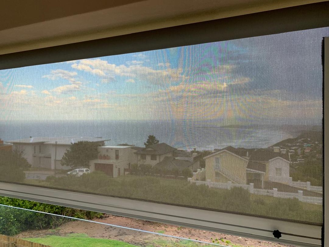 The sea seen through a lowered sidetrack screen mesh outdoor blind, by Custom Blinds Shutters & Awnings, Knysna