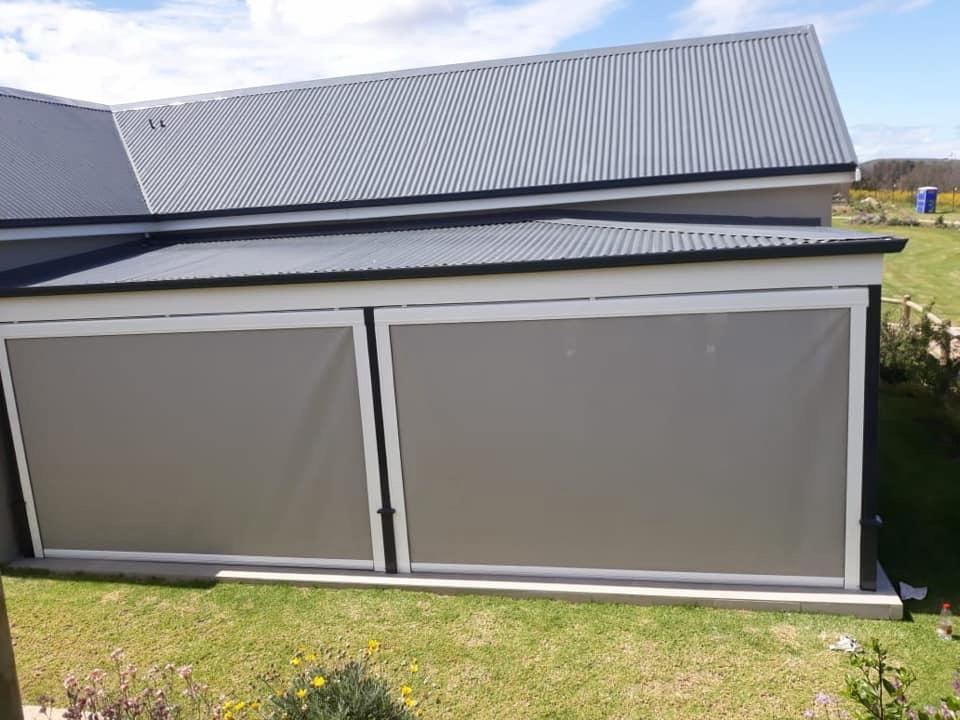 Two grey sidetrack outdoor blinds lowered in white aluminium side channels on a covered patio, by Custom Blinds Shutters & Awnings, Knysna