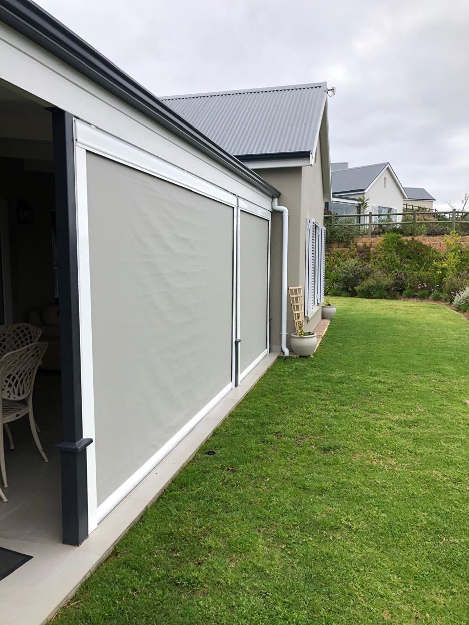 Grey sidetrack outdoor blinds closed along the edge of a covered patio, by Custom Blinds Shutters & Awnings, Knysna